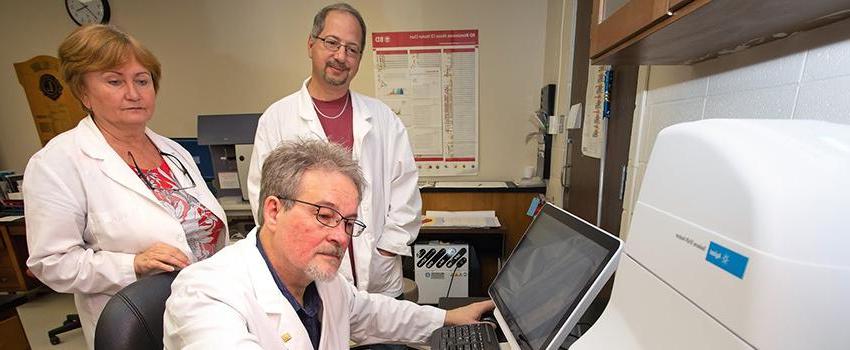 Mikhail Alexeyev, Ph.D., professor of physiology and cell biology at the USA College of Medicine, places a sample in the Seahorse XFe24 extracellular flux analyzer as Domenic Spadafora, Ph.D., manager of the flow cytometry facility at the USA College of Medicine, and research technician Nataliya Kozhukhar look on.